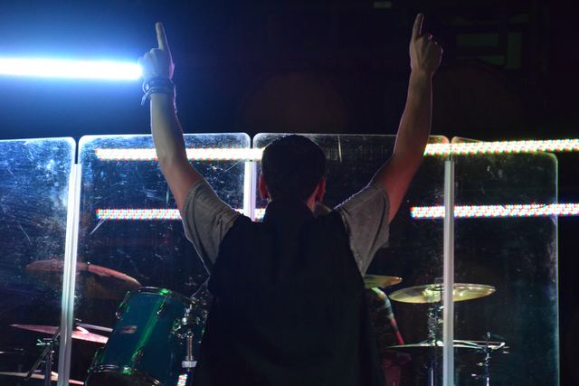 Silhouette of a band member with both arms raised against the stage lights
