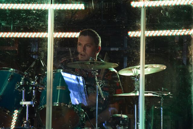 Drummer behind the kit and shield, lit green