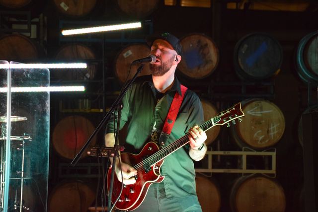 Guitarist playing, green light washing the barrel room behind
