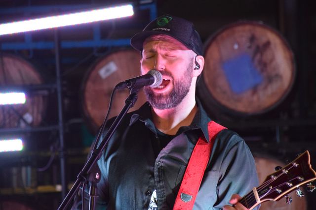 Guitarist singing into the mic, lit purple against a wall of barrels