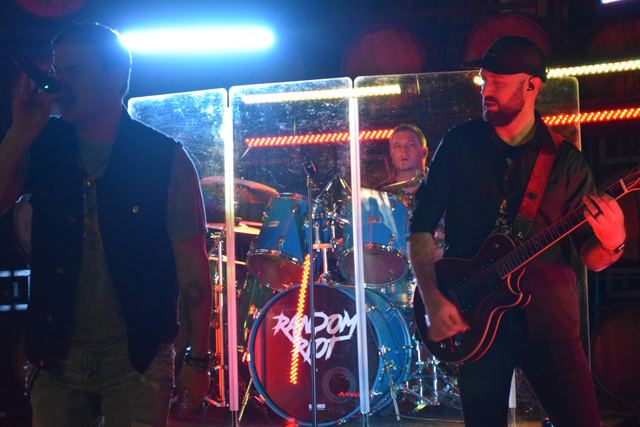 Three of the band playing together, blue and red light across the stage