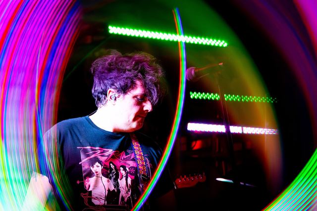 Guitarist mid-song, ringed by streaks of coloured stage light