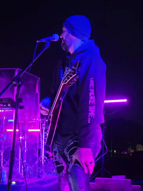 Singer at the mic in a beanie, lit magenta against the night
