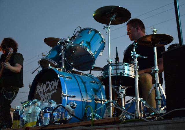 The drummer behind a blue kit at an outdoor daytime show